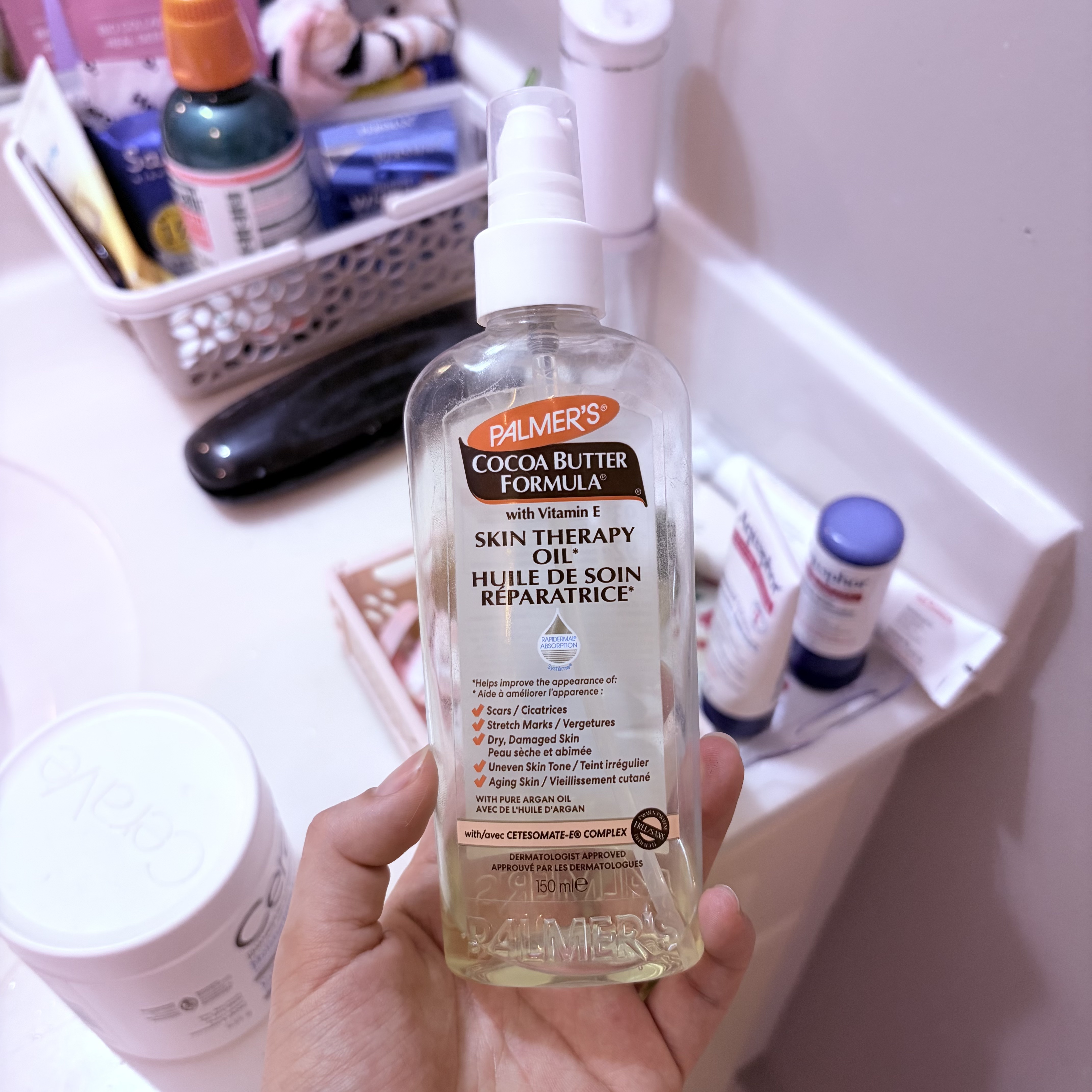 A family member’s hand holding an almost-empty 150 mL bottle of Palmer’s Skin Therapy Oil in the bathroom